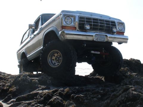 1978 Ford Bronco - Modified 1978 Ford Bronco navigating a rocky shoreline with large off-road tires.