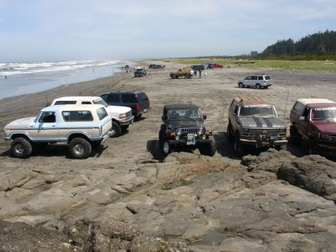 1978 Ford Bronco - A group of off-road vehicles gathered on a rocky shoreline with the ocean in the background.