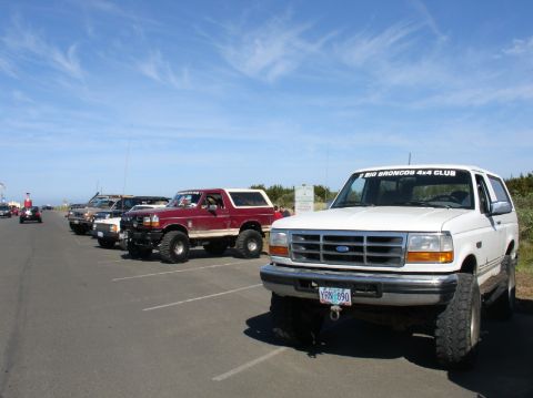 1978 Ford Bronco - Several Ford Bronco SUVs are parked in a lot under a blue sky with scattered clouds.