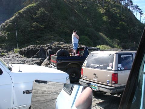 1978 Ford Bronco - A man stands on the bed of a black Ford Bronco parked on a beach, with other vehicles nearby.