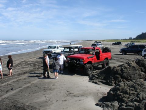 1978 Ford Bronco - Several off-road vehicles are parked on a beach near the ocean.