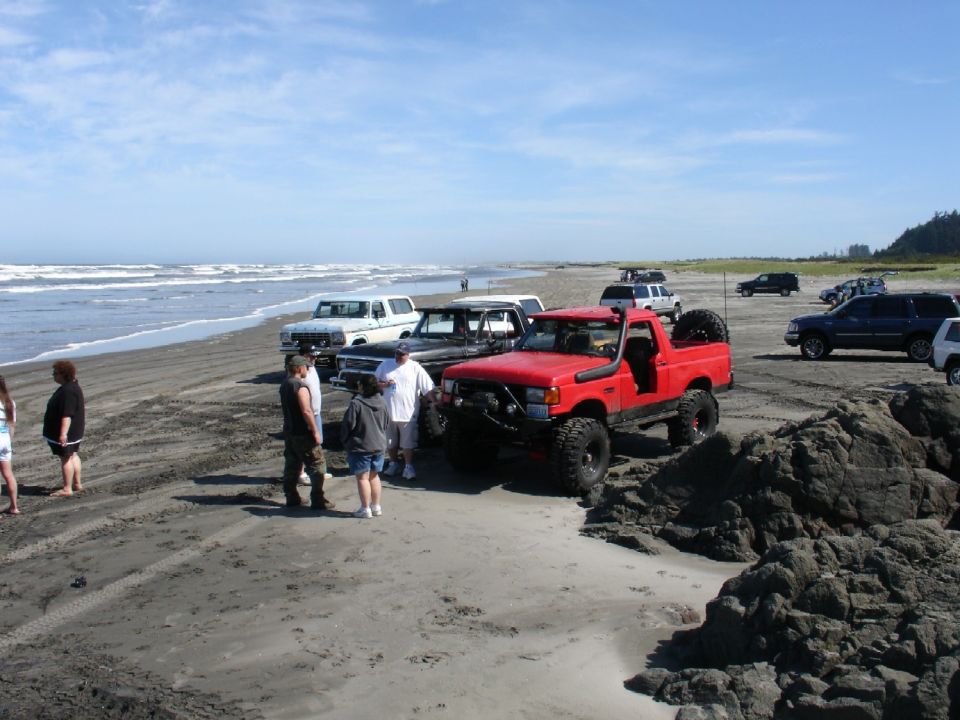 Red Ford Bronco with large tires and snorkel on a sandy beach