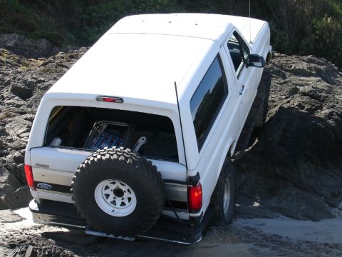 1978 Ford Bronco - White Ford Bronco driving over rocks and sand, showing its off-road capability.