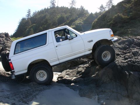 1978 Ford Bronco - White Ford Bronco navigates rocky terrain near a beach.