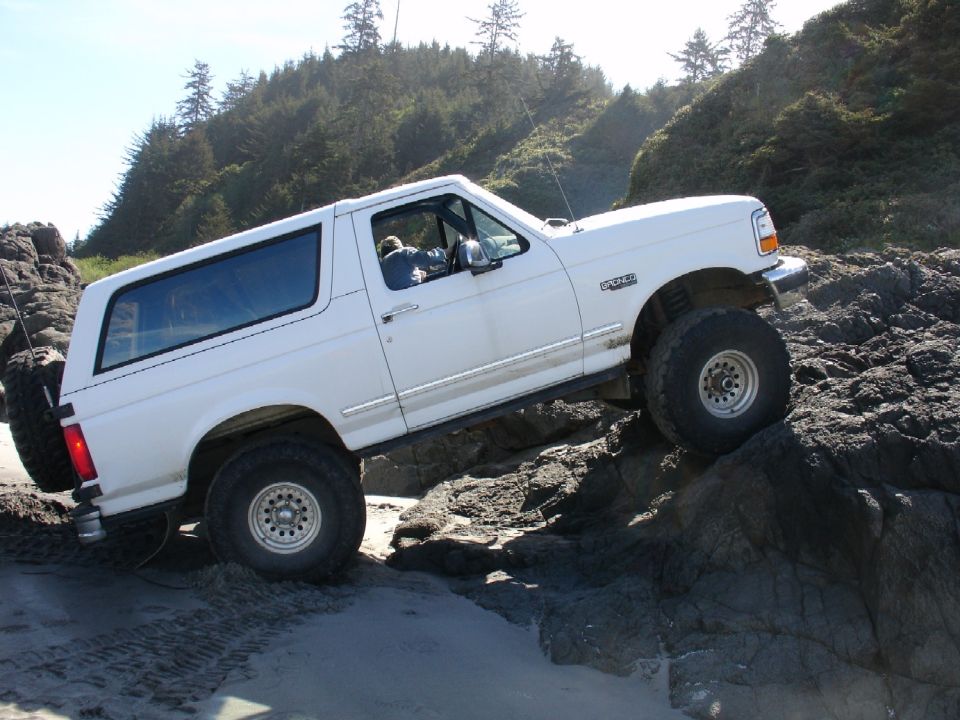 White Ford Bronco on rocks, spare tire on rear, driver visible