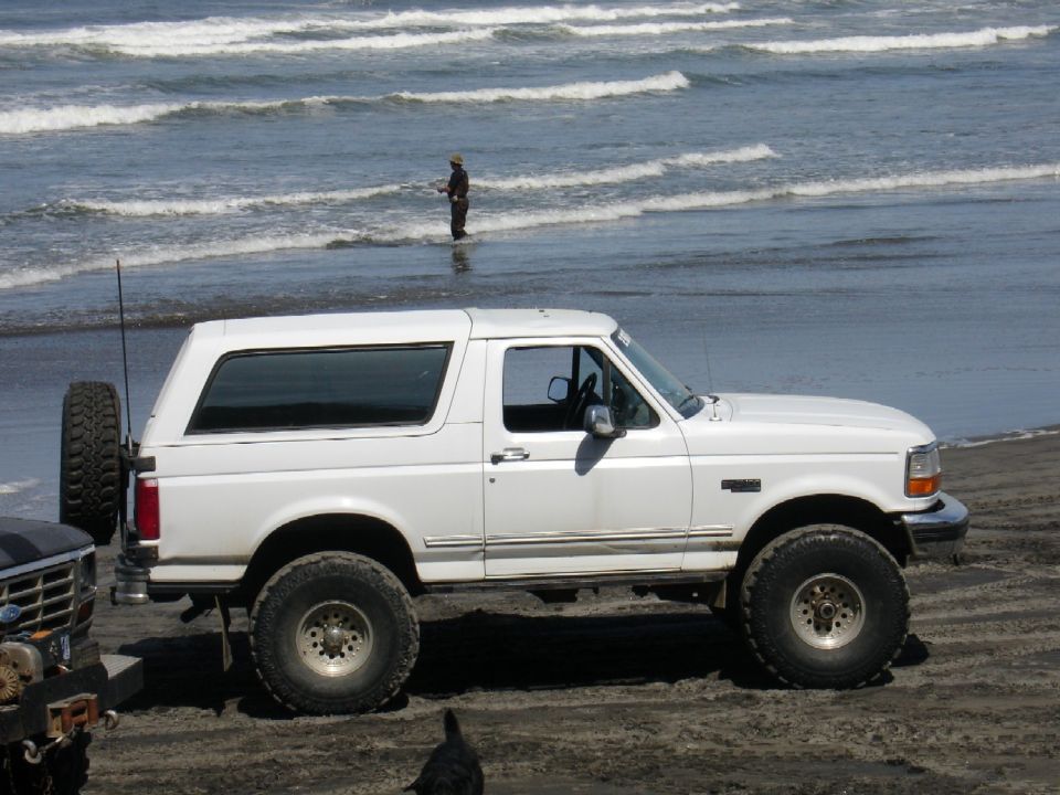 White Ford Bronco parked on a sandy beach with ocean waves in the background