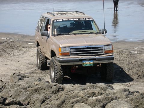 1978 Ford Bronco - Ford Explorer with off-road tires navigating a rocky beach, with a club sticker on the windshield.