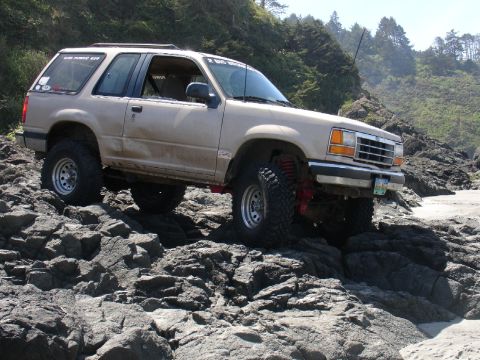 1978 Ford Bronco - This lifted SUV is shown navigating a rocky beach, demonstrating its off-road capabilities.
