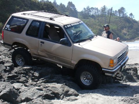 1978 Ford Bronco - Ford Explorer tackling rocky beach terrain, despite "2 BIG BRONCOS BEACH RUN" sticker on windshield.