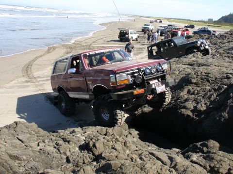 1978 Ford Bronco - Several off-road vehicles navigate a rocky shoreline on a sunny day.