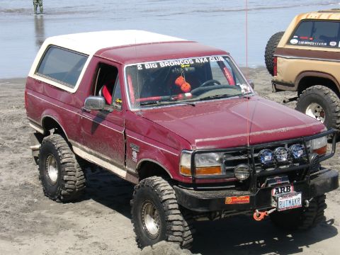 1978 Ford Bronco - Modified Ford Bronco with off-road tires parked on a beach next to another Bronco.