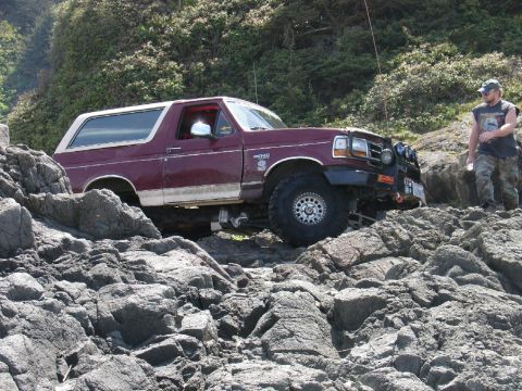 1978 Ford Bronco - A maroon Ford Bronco navigates a rocky coastal path with a man standing nearby.