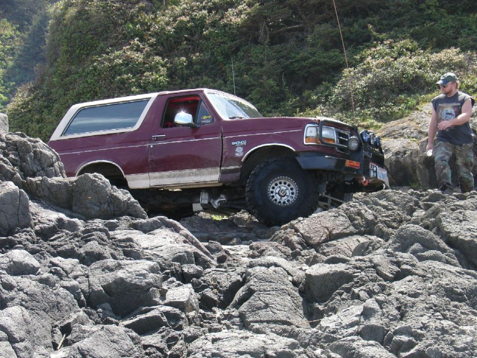 Maroon Ford Bronco with white top on rocky terrain, driver's side visible