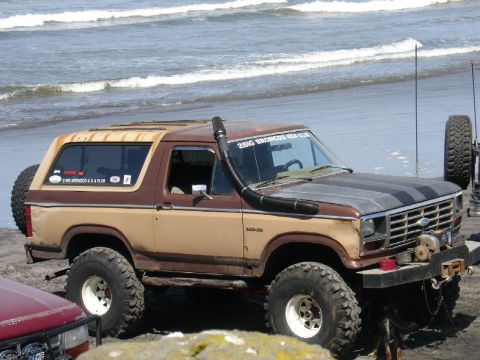 1978 Ford Bronco - Modified 1978 Ford Bronco parked on the beach near the ocean waves, with a snorkel and off-road tires.