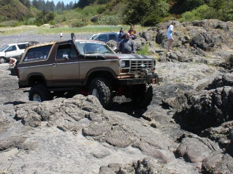 1978 Ford Bronco - Two-tone Ford Bronco navigates a rocky beach with other vehicles nearby.
