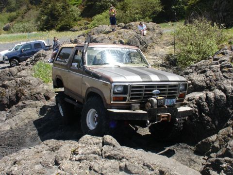1978 Ford Bronco - A lifted 1978 Ford Bronco navigates a rocky coastal terrain, with other vehicles visible in the background.