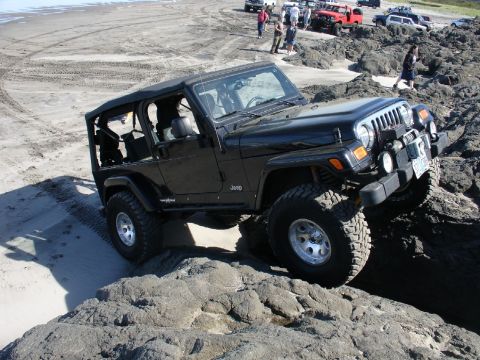 1978 Ford Bronco - A group of off-road vehicles tackle a rocky beach terrain.