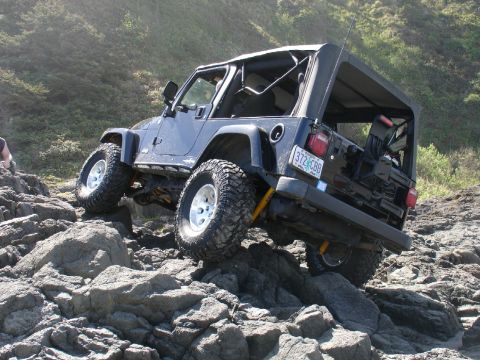 1978 Ford Bronco - A dark blue Jeep Wrangler navigates a rocky coastal path.