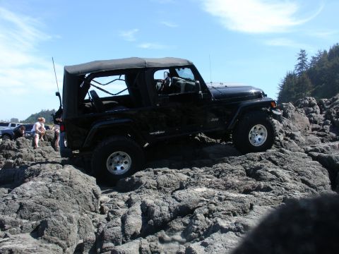 1978 Ford Bronco - A black Jeep Wrangler navigates a rocky coastal path with other vehicles and people nearby.