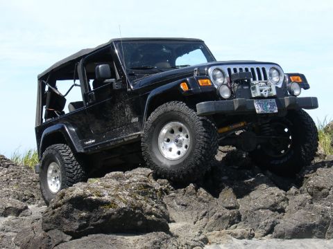 1978 Ford Bronco - Jeep Wrangler TJ navigating a rocky trail under a clear blue sky.