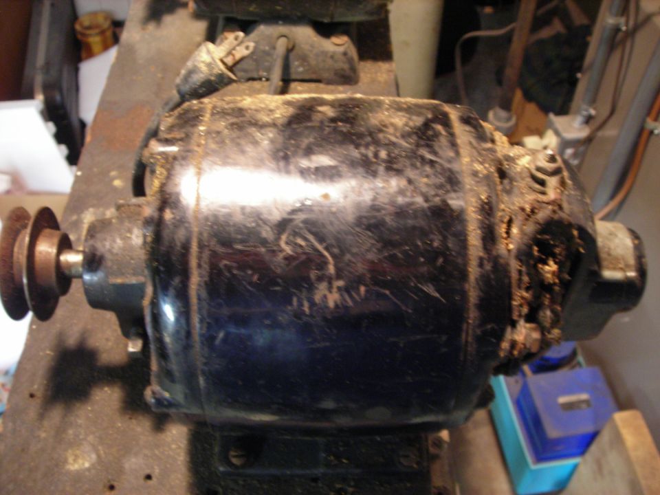 Black electric motor with a two-pulley system, covered in dust and debris