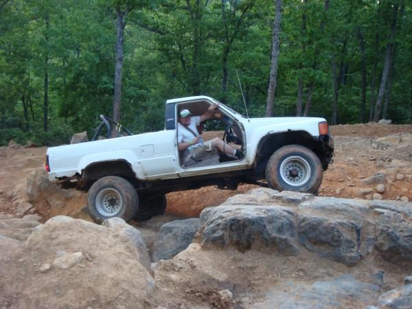 White pickup truck with off-road tires navigating large rocks on a dirt trail
