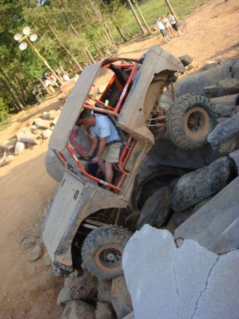 1978 Ford Bronco - A person works on an off-road vehicle that has become stuck on a pile of large rocks.