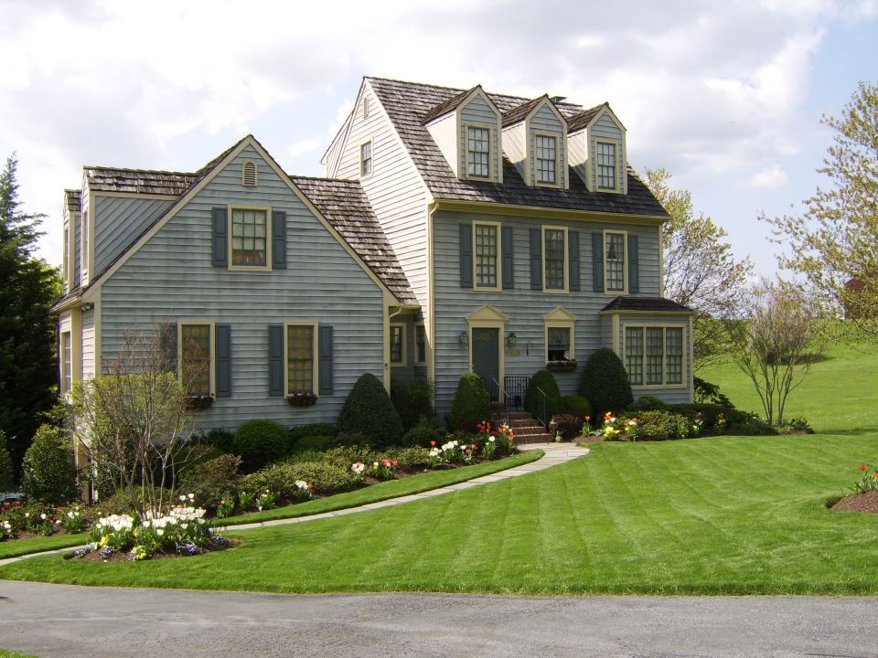 Blue clapboard colonial house with dormers, tulip beds and manicured lawn