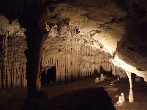 1979 Ford Bronco - A view inside a cave, illuminated to reveal numerous stalactites and stalagmites, with a website logo visible in the lower right corner.