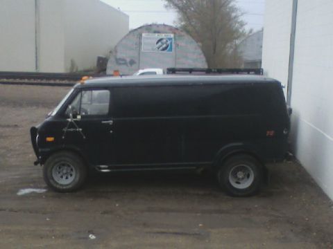 1992 Ford F-350 - A black panel van is parked on a dirt lot next to a white building. The van appears to be modified for off-road use.