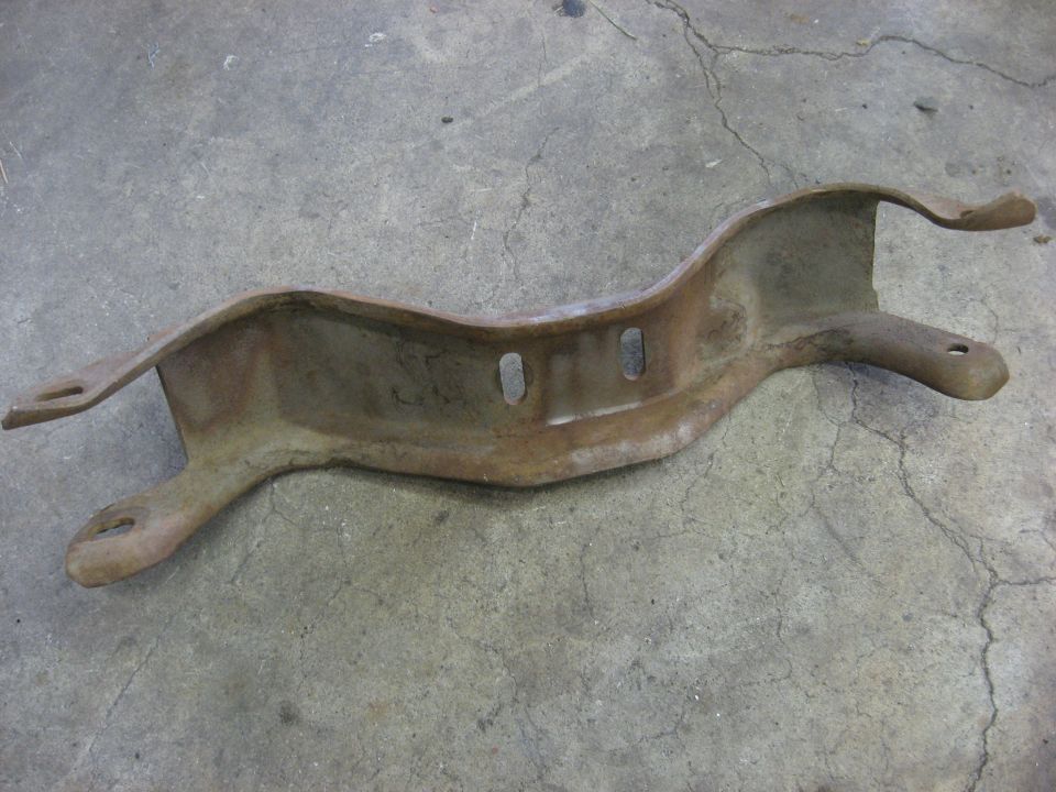 Rusty metal bracket with two mounting holes on each end, resting on a concrete floor
