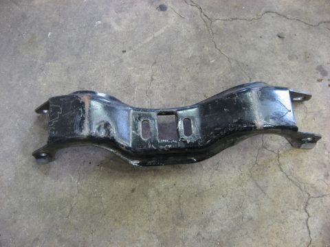 1978 Ford Mustang II - Black metal automotive part, possibly a crossmember or support, photographed on a concrete surface.