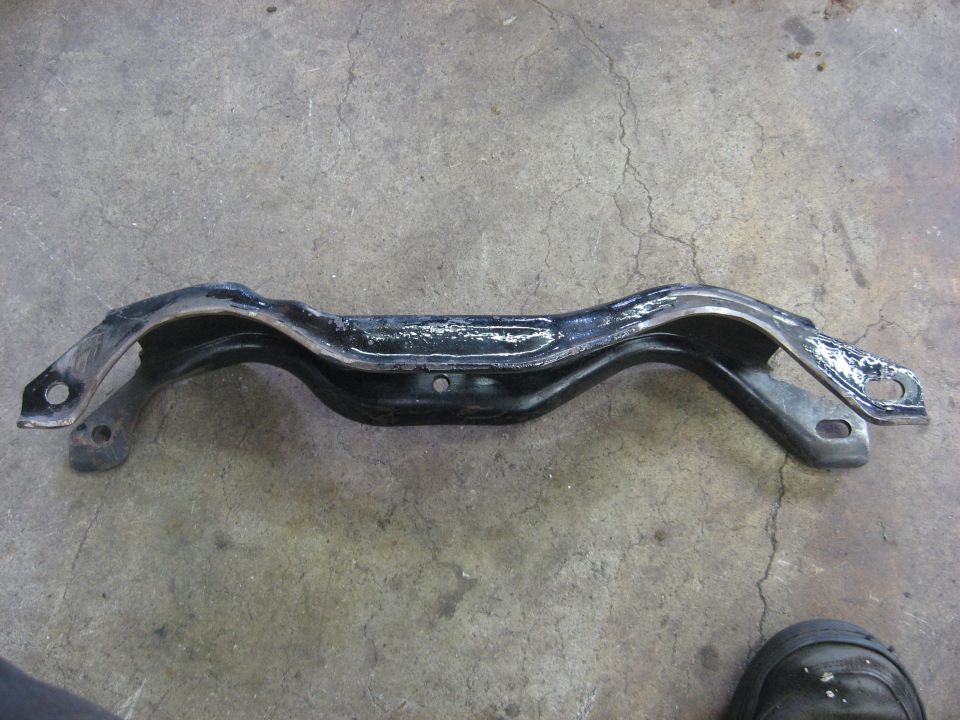 Black metal automotive crossmember with mounting holes on a concrete floor