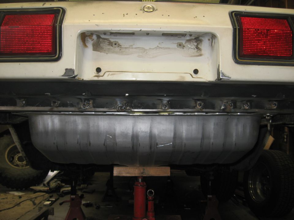 White car rear with red taillights and a new metal gas tank mounted underneath