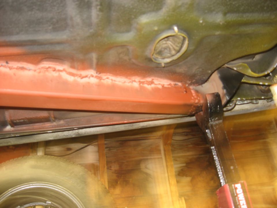 Underbody view of vehicle with red frame rail and tire; jack visible