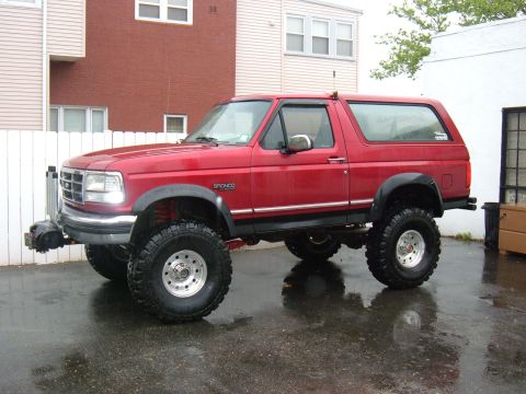 1994 Ford Bronco - This lifted Ford Bronco is parked on a wet surface, showing its side profile and large off-road tires.