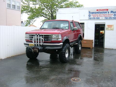1994 Ford Bronco - A red Ford Bronco with custom front grille and lifted suspension is parked outside a repair shop.