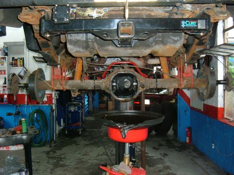 1994 Ford Bronco - Underside view of a truck on a lift with the rear differential cover removed and gear oil draining into a red catch pan below. The solid re…