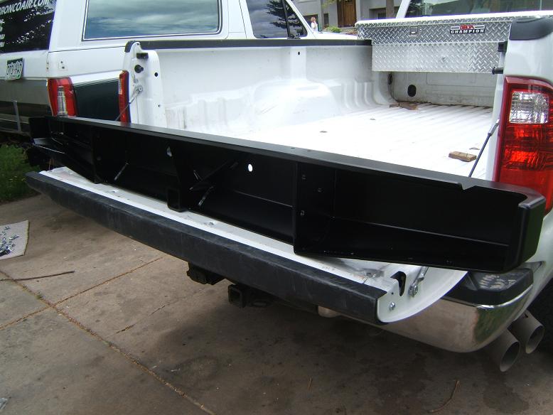 Black aftermarket rear bumper installed on a white pickup truck bed