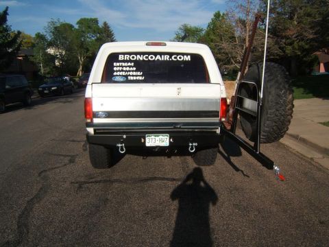 1993 Ford Bronco - Rear view of a white Ford Bronco a spare tire carrier and aftermarket bumper. The window displays a BroncoAir.com sticker.