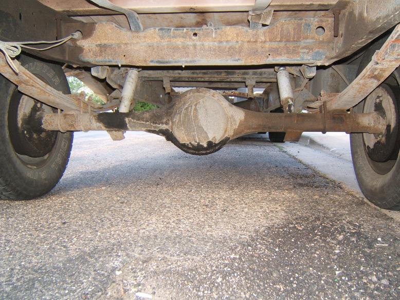 Rear underbody view of rusty solid axle, differential, leaf springs and rear tires