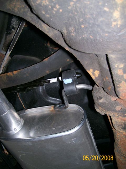 1995 Mercury Grand Marquis - Under-car close-up of a new bright muffler hung from a black rubber isolator, its welded hanger rod hooked into the mount alongside the rus…