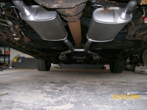 1995 Mercury Grand Marquis - Underside view of a vehicle showing a dual exhaust system with two large polished stainless steel mufflers, connected piping, and a rusted…