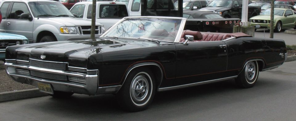 Black 1960s Mercury convertible with red interior in a parking lot