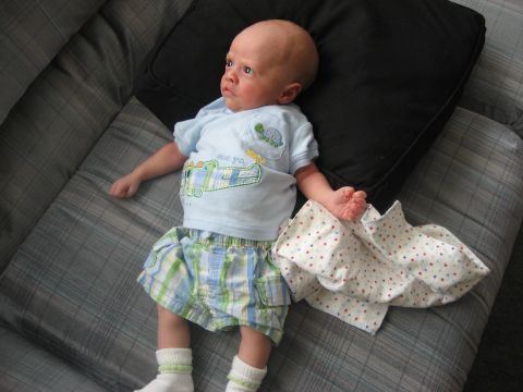 1981 Ford Bronco - A baby is lying on a couch, dressed in a blue shirt and plaid shorts.