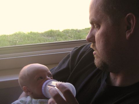 1981 Ford Bronco - A man feeds a baby from a bottle while looking out a window.