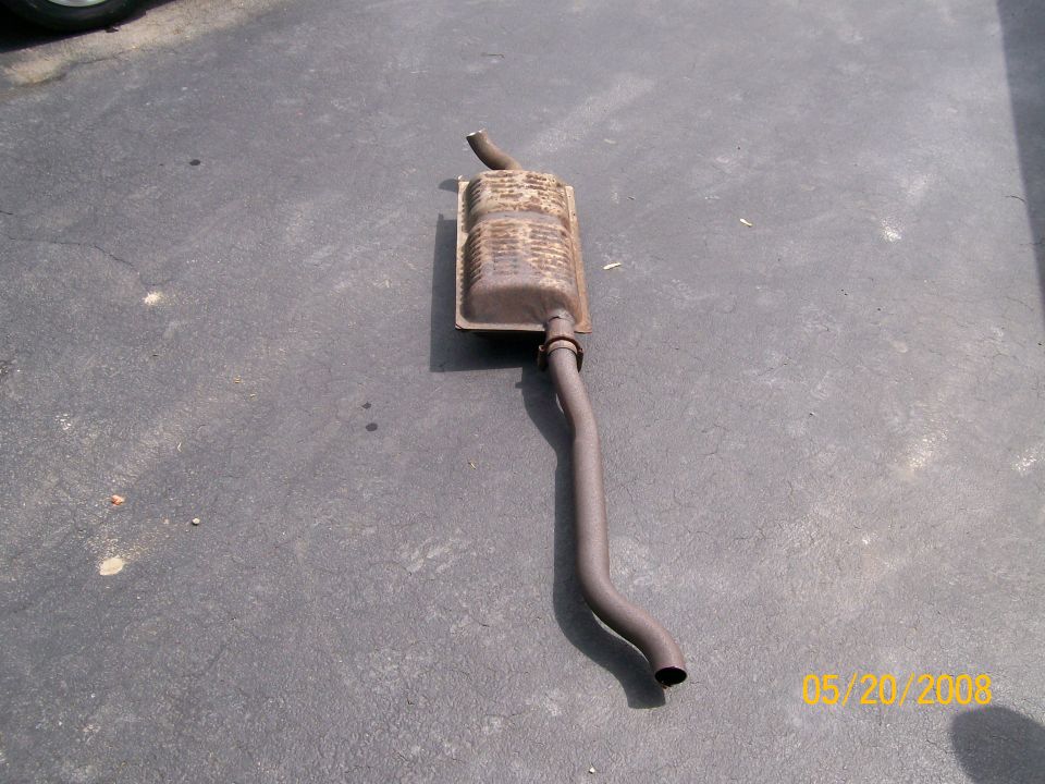 Rusty removed oval muffler with bent tailpipe lying on asphalt