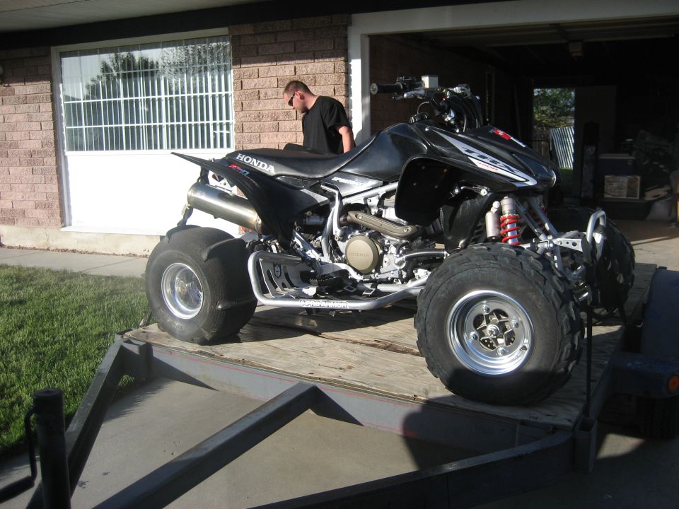 Black ATV with silver exhaust and red shocks on a trailer