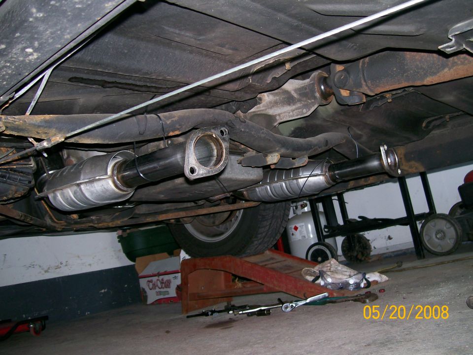 Two new stainless catalytic converters installed under a car on ramps