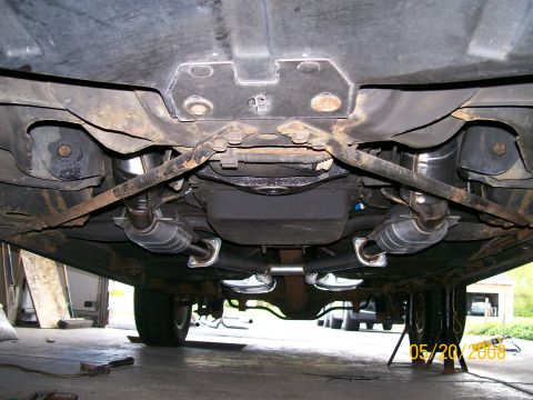 1995 Mercury Grand Marquis - Underbody view from behind a car raised on jack stands, showing a newly installed dual exhaust system with two polished stainless catalytic…